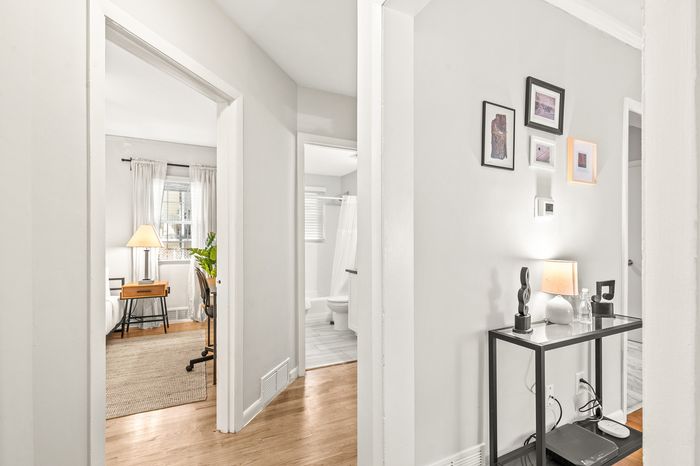 Bright and inviting apartment hallway leading to a beautifully decorated bedroom and modern bathroom, featuring elegant wall art and cozy lighting.