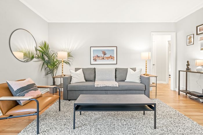 Inviting living room with modern gray sofa, stylish leather chair, and elegant decor, accented by lush greenery and warm lighting.
