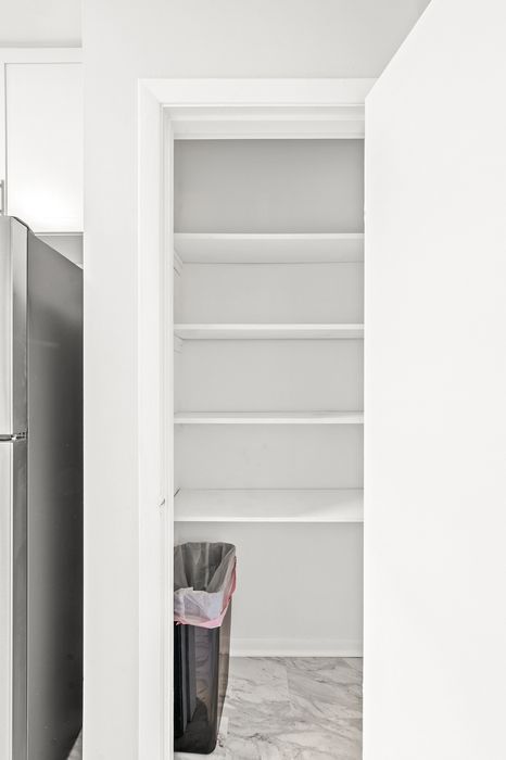 Sleek and modern pantry space with built-in shelving, adjacent to a stainless steel refrigerator, offering ample storage for an organized kitchen.