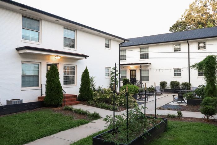Charming apartment exterior with inviting courtyard, lush greenery, and cozy seating area perfect for relaxation.