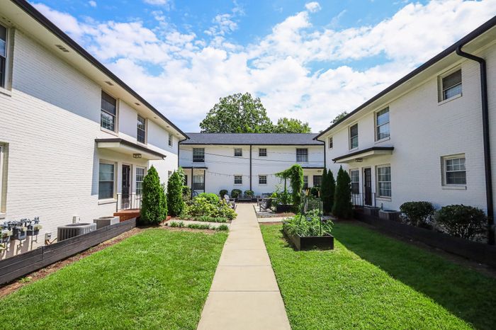 Charming courtyard in a modern apartment complex, featuring manicured gardens and vibrant green spaces under a clear blue sky.