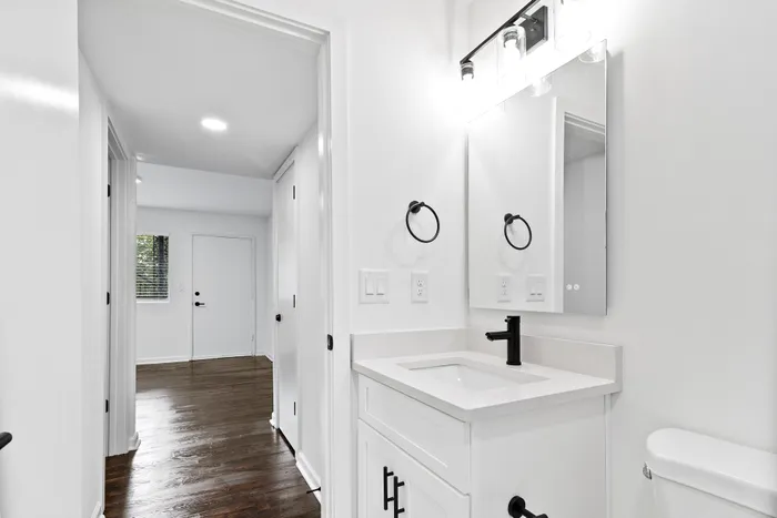 Elegant bathroom with sleek black fixtures and a modern vanity, leading into a bright hallway with rich wooden floors.