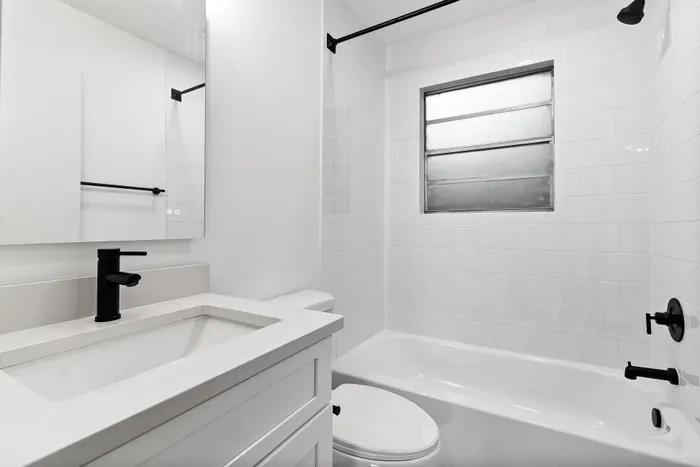 Elegant bathroom with a modern monochrome design, featuring a sleek white vanity, matte black fixtures, and a tastefully tiled bathtub area.