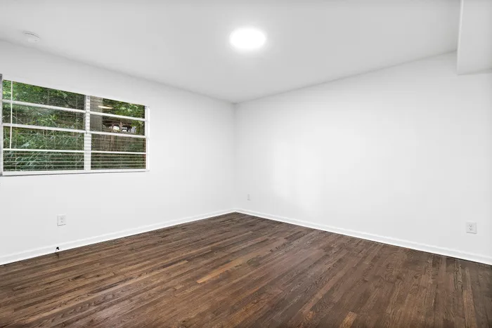 Bright and airy room with elegant hardwood flooring, large window showcasing lush greenery.
