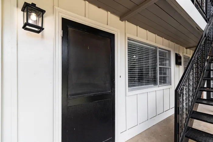 Welcoming apartment entrance with a modern black door and charming outdoor light fixture.