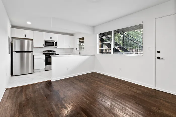Bright and modern kitchen with sleek stainless steel appliances, elegant white cabinetry, and a large window offering a view of the outdoors. The space features stylish hardwood flooring and ample natural light.