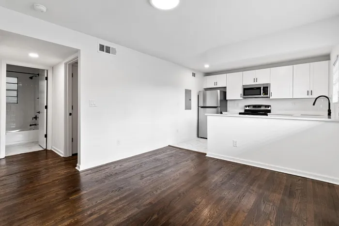 Modern apartment with sleek hardwood floors and a bright open-concept kitchen featuring white cabinets and stainless steel appliances.