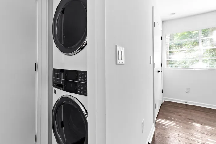 Contemporary laundry nook featuring a sleek stacked washer and dryer in a bright and airy hallway with hardwood flooring.