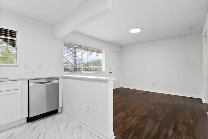 Chic open-plan kitchen and living area with sleek stainless steel appliances and large windows offering natural light, creating a bright and airy space.