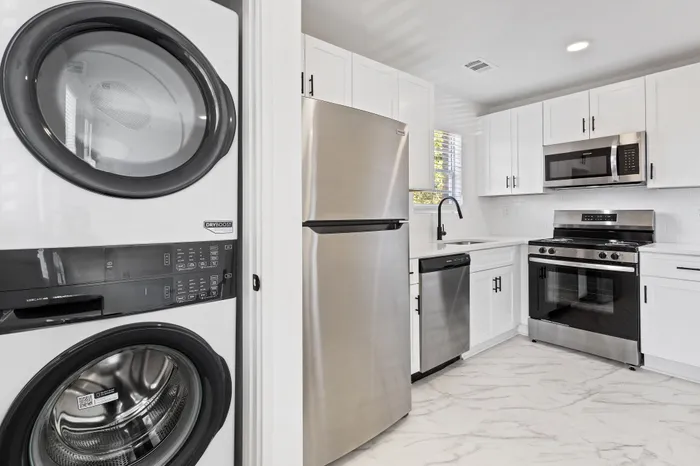 Sleek modern kitchen featuring stainless steel appliances, marble flooring, and an in-unit washer dryer.