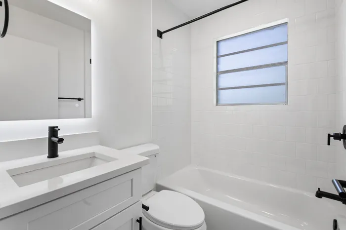 Bright, modern bathroom with sleek white fixtures, elegant black accents, and a large frosted window for natural light.