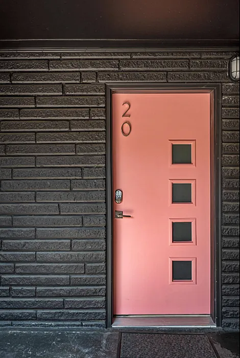 Chic entrance with a bold pink door featuring modern geometric glass panels against a sleek dark brick wall, creating a contemporary and welcoming entryway.