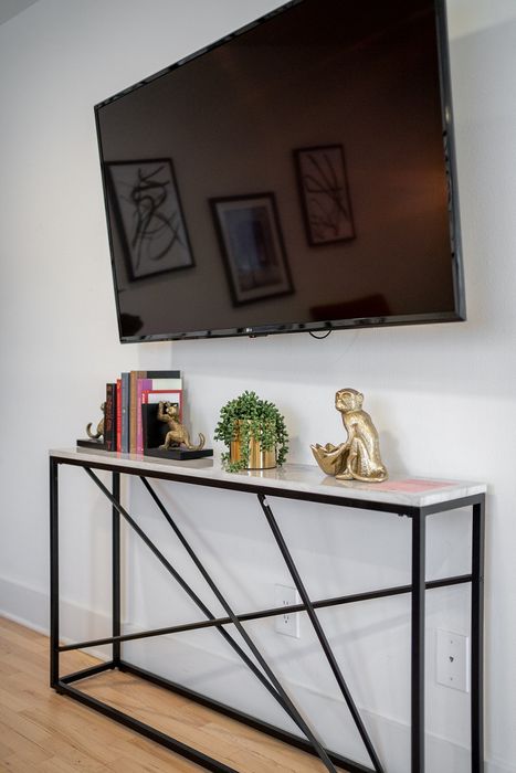 Chic living room setup with a sleek wall-mounted TV, stylish console table adorned with books, gold monkey figurines, and a lush potted plant on a wooden floor.