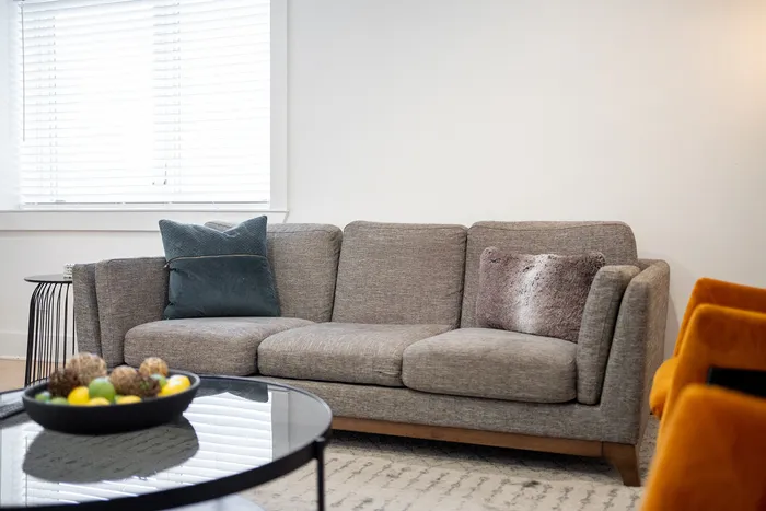 Cozy and modern living room with a plush gray sofa, vibrant cushions, and a stylish glass coffee table adorned with decorative accents.