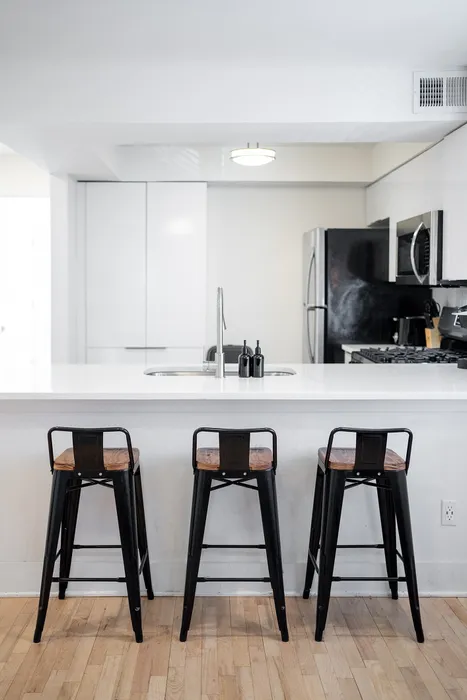 Sleek modern kitchen with a bright white island, three stylish metal bar stools, and stainless steel appliances.