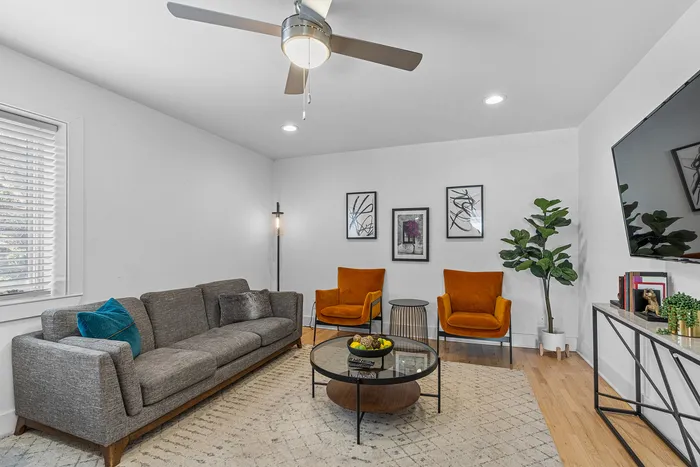 Charming living room with a modern grey sofa, vibrant orange chairs, stylish glass coffee table, and elegant decor, perfect for relaxation and entertainment.