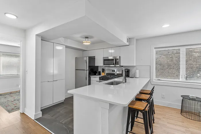 Modern and inviting kitchen with sleek white cabinetry, stainless steel appliances, and a chic breakfast bar with stylish seating.