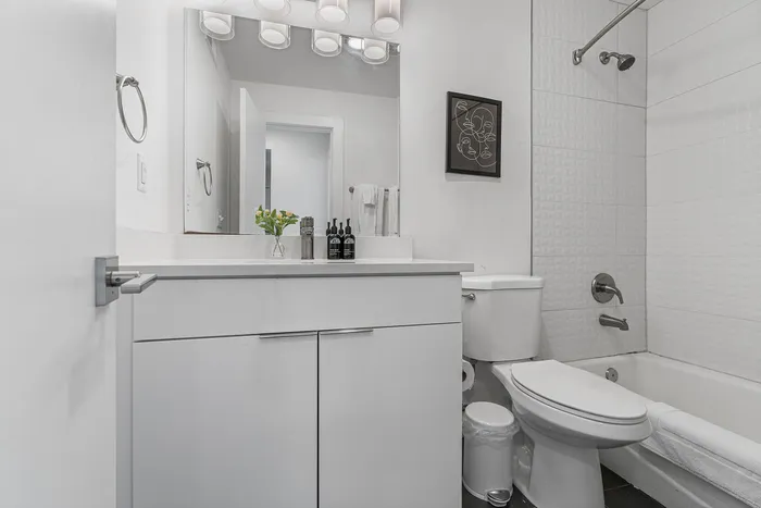Modern bathroom with sleek white vanity, large mirror, elegant lighting, and a contemporary bathtub offering a clean, sophisticated ambiance.
