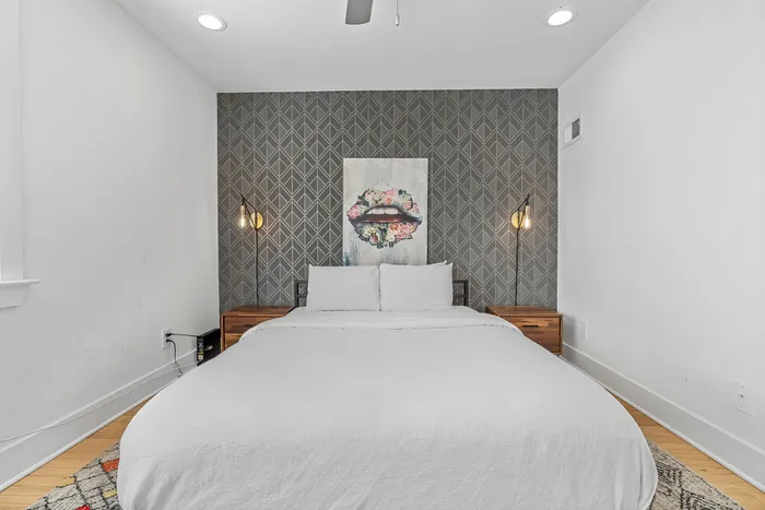 Chic bedroom with elegant wallpaper, soft lighting, and modern artwork above a cozy bed.