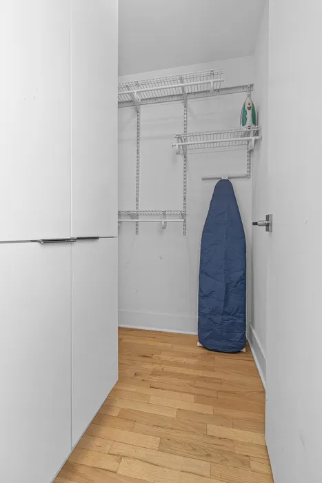 Modern closet with sleek shelving, ample storage space, and hardwood flooring, featuring an ironing board and iron for convenience.