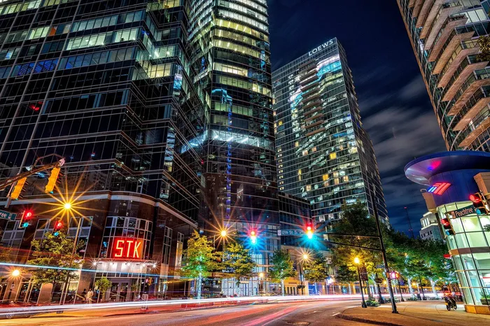 Vibrant cityscape at night with illuminated modern high-rise buildings, bustling street lights, and glowing storefronts, creating a lively urban atmosphere.