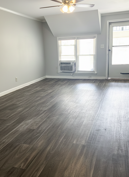 Bright and airy room with sleek hardwood flooring, modern ceiling fan, and abundant natural light from large windows.