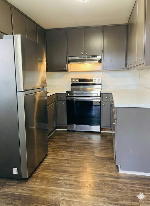 Modern kitchen with sleek stainless steel appliances, elegant dark cabinetry, and polished hardwood floors.