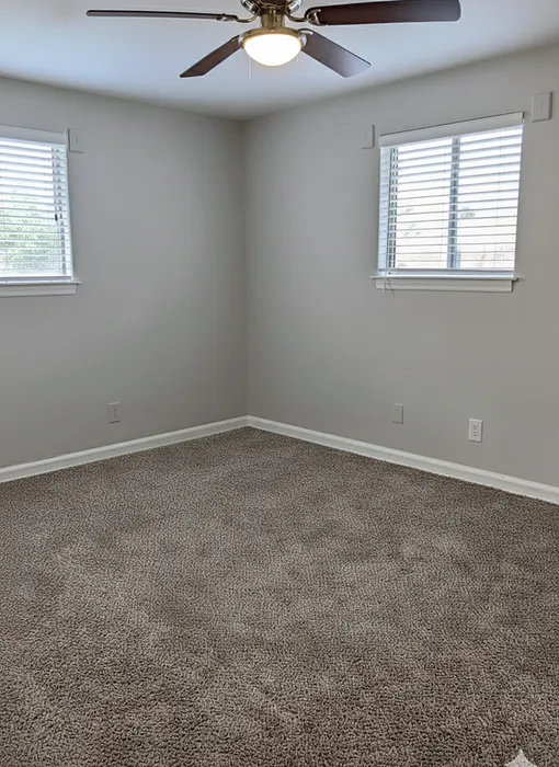 Bright and airy bedroom with plush carpet, dual windows for natural light, and a modern ceiling fan.