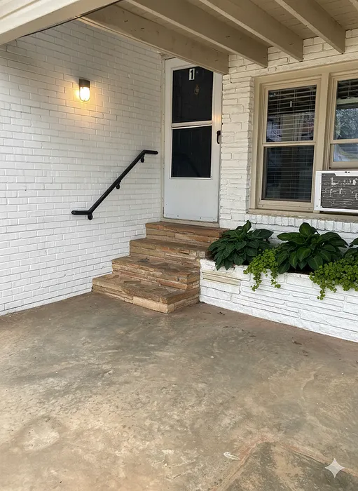 Charming apartment entrance with rustic stone steps, modern light fixture, and vibrant greenery on a cozy porch.