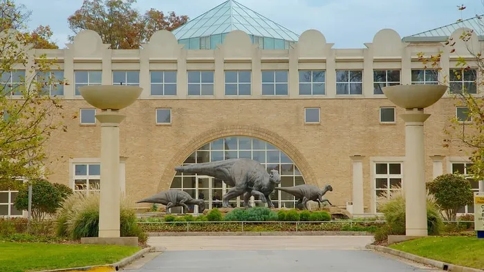 Majestic building facade with striking dinosaur sculptures on display in a beautifully landscaped area.