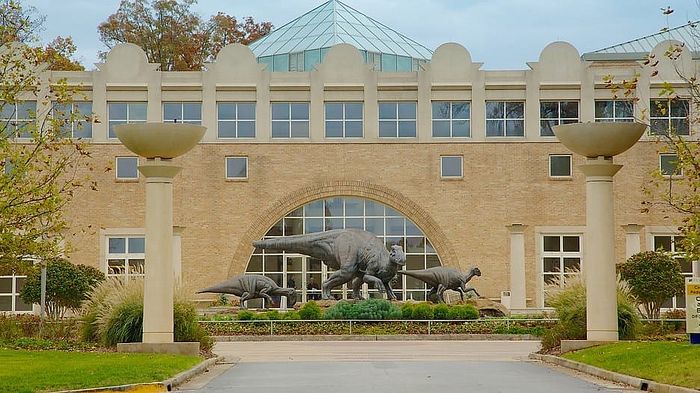Elegant building facade with impressive dinosaur sculptures and lush landscaping, creating a striking architectural display.