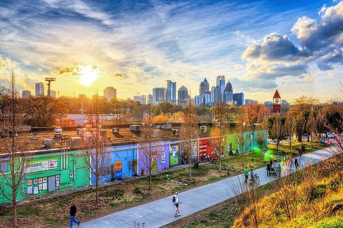 Vibrant cityscape during golden hour showcasing a lively park with people walking and cycling, surrounded by colorful buildings and a breathtaking skyline.