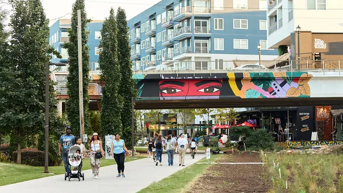 Vibrant urban living scene with people enjoying a lively pedestrian walkway, complemented by colorful street art and modern apartment buildings in the background.