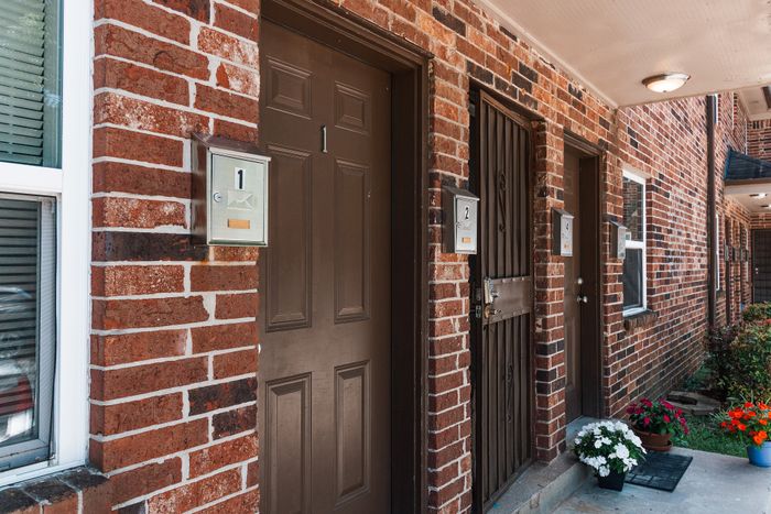 Charming brick apartment entrance featuring bold red brick walls, stylish doors, and vibrant potted flowers.