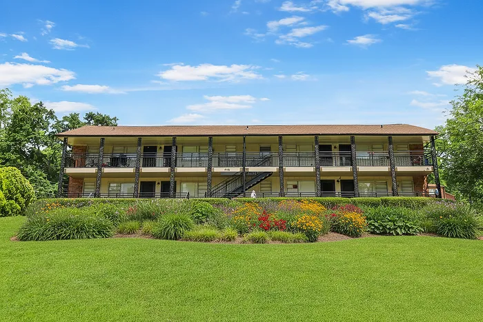 Charming two-story apartment building with lush landscaping and vibrant flowers under a clear blue sky.