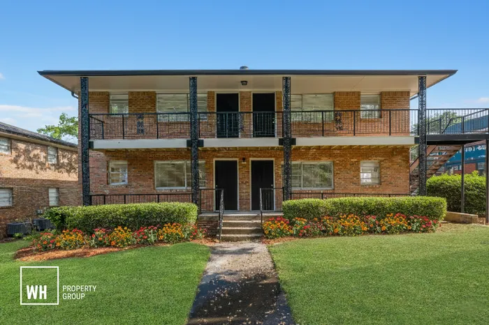 Charming brick apartment building with landscaped gardens and inviting front porches, perfect for relaxed living.