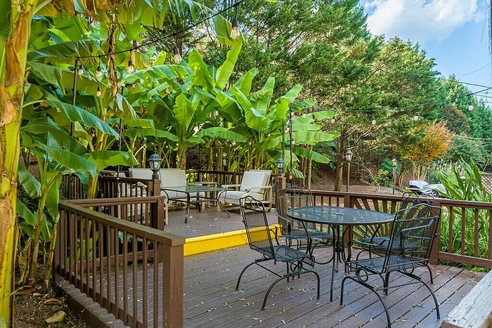 Charming outdoor deck with lush greenery, featuring elegant seating and ambient string lights for a perfect relaxation spot.