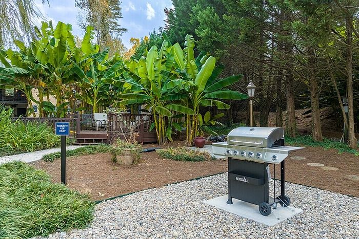 Charming outdoor space featuring a sleek barbecue grill, surrounded by lush greenery and tropical banana trees, perfect for resident relaxation.