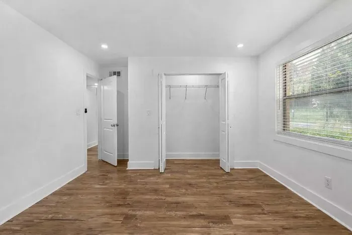 Bright and spacious bedroom with elegant wooden flooring, large window for natural light, and a convenient built-in closet.