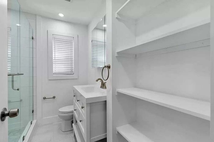 Bright and modern bathroom featuring sleek glass shower, elegant sink, and ample built-in shelving.