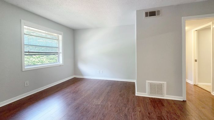 Bright and airy room with elegant hardwood flooring, large window inviting natural light, and smooth, modern walls.