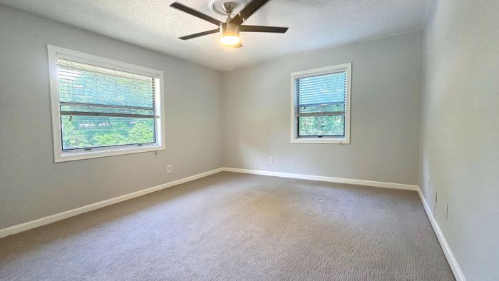 Bright and spacious bedroom with dual windows, modern ceiling fan, and soothing neutral tones.