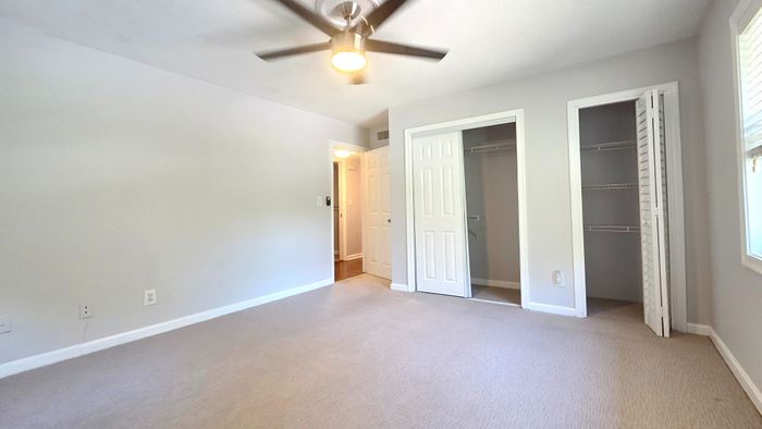 Bright, serene bedroom featuring a spacious closet, plush carpeting, and modern ceiling fan.