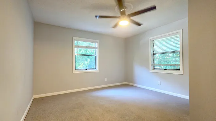 Bright and airy bedroom with large windows, neutral walls, and a modern ceiling fan, perfect for relaxation.