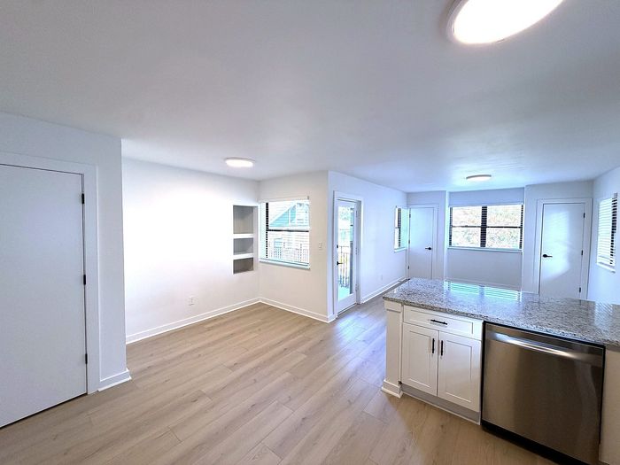 Bright and modern open-concept living area with sleek wooden flooring, showcasing a chic kitchen with granite countertops and ample natural light.