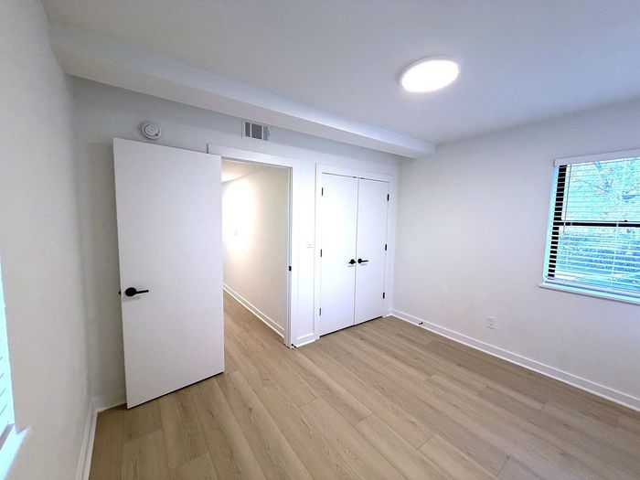Bright and airy bedroom with sleek wood-look floors, a large window for natural light, and modern closet doors.