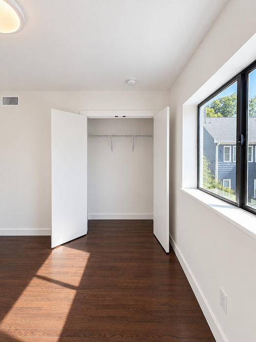 Bright and airy room with sleek hardwood floors and a large modern closet, featuring abundant natural light through a big window.