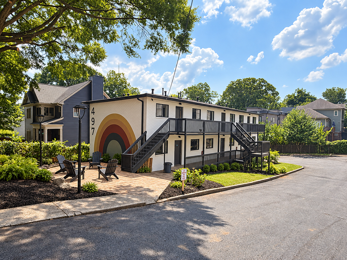 Charming apartment building with vibrant rainbow mural, featuring outdoor seating, lush landscaping, and a tranquil setting.