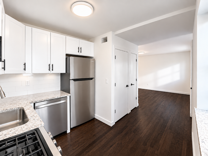Modern kitchen with sleek stainless steel appliances, white cabinetry, and elegant dark wood flooring leading into a bright living space.