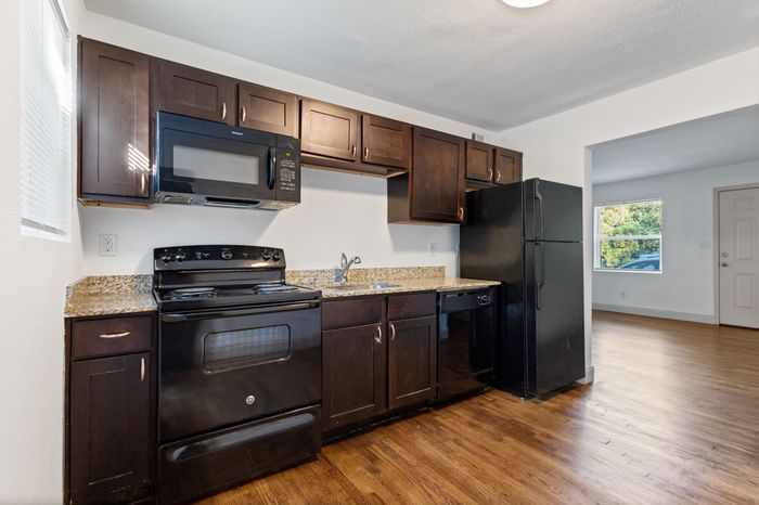 Modern kitchen with dark wood cabinetry, sleek black appliances, and elegant granite countertops in a spacious apartment.